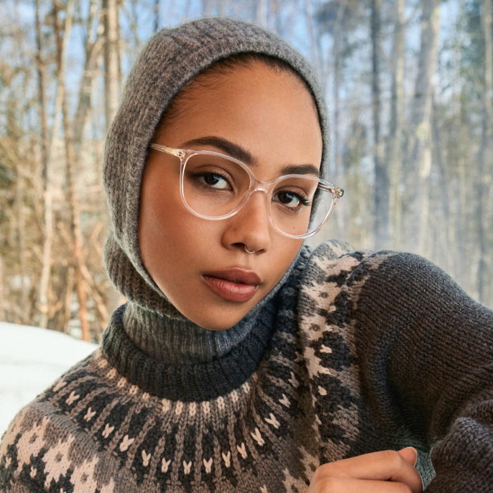 Person wearing glasses and a knitted sweater, with a forest background.