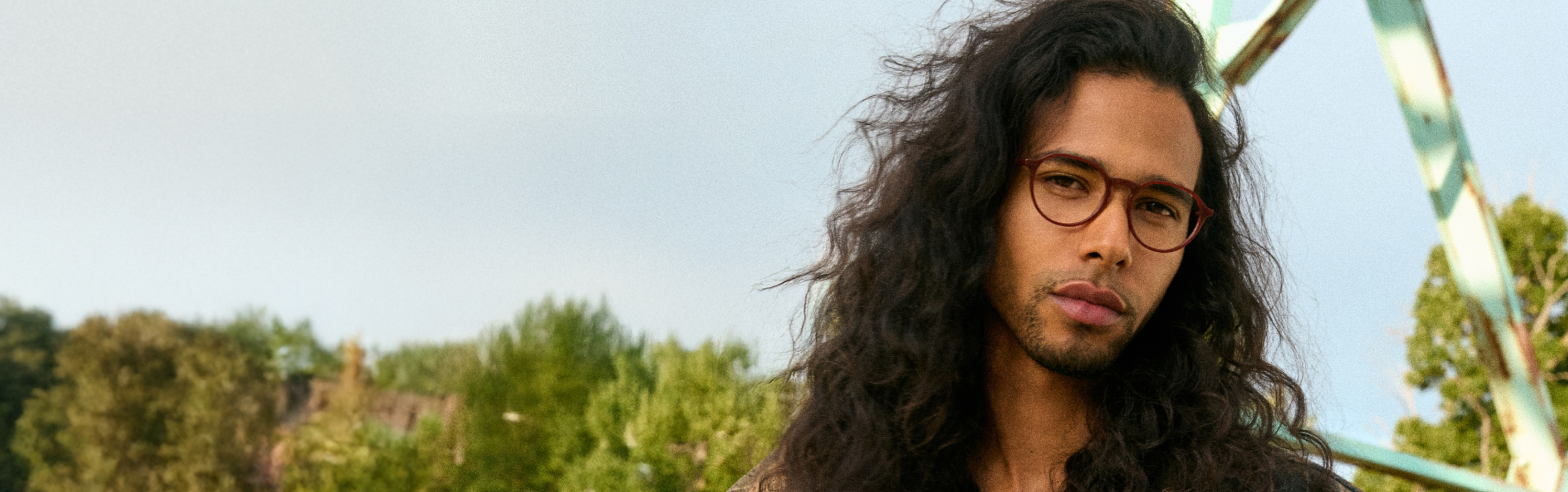 Person with long hair and glasses outdoors, trees in background.