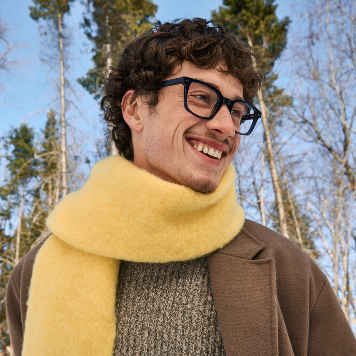 Smiling person wearing glasses and a yellow scarf outdoors.