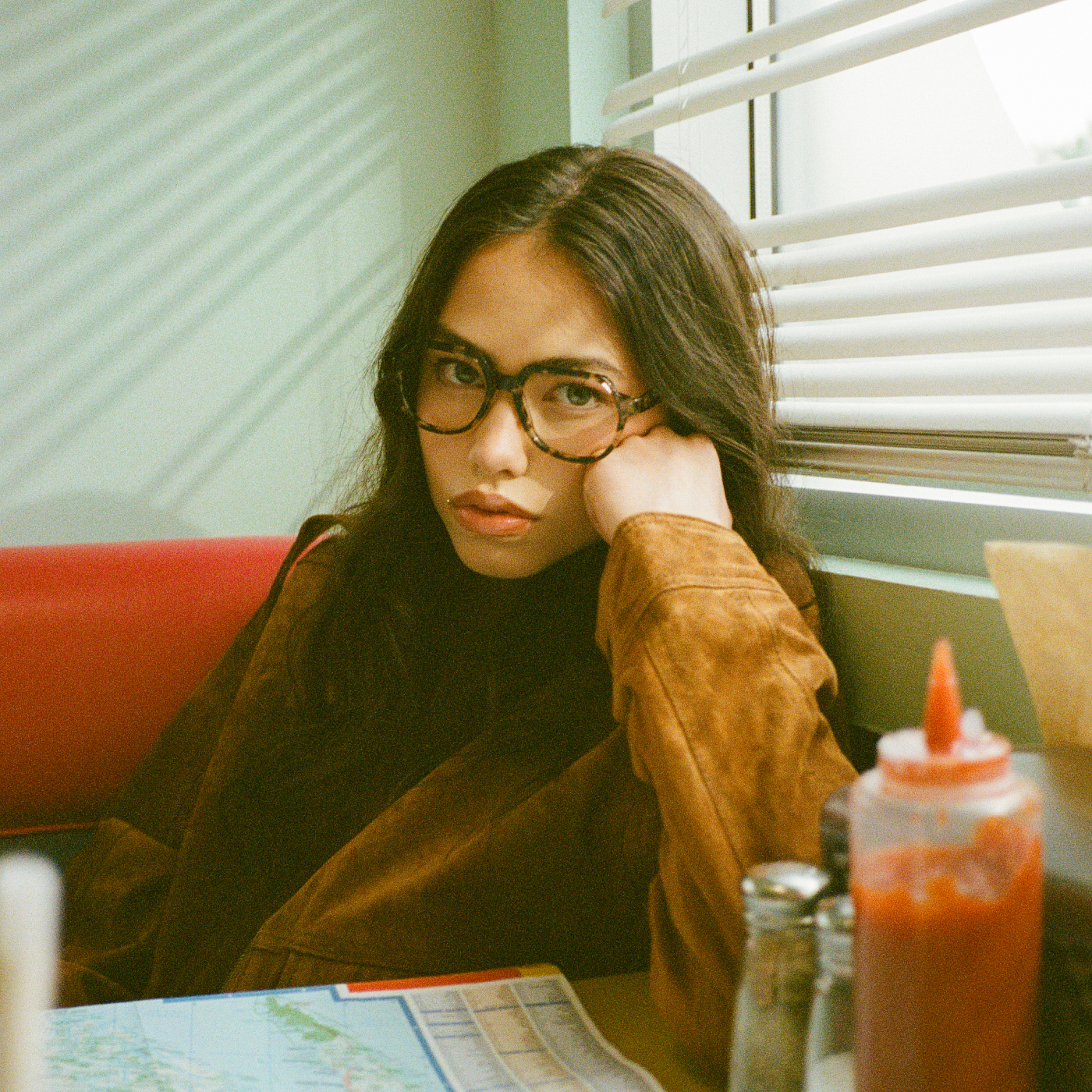 Person with glasses sitting in a diner booth, leaning on hand.