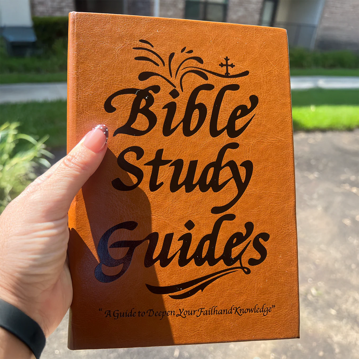 A person's hand holding a brown book titled 'Bible Study Guides'.