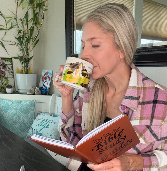 A person with blonde hair in a plaid shirt sips from a mug while reading a Bible study guide.