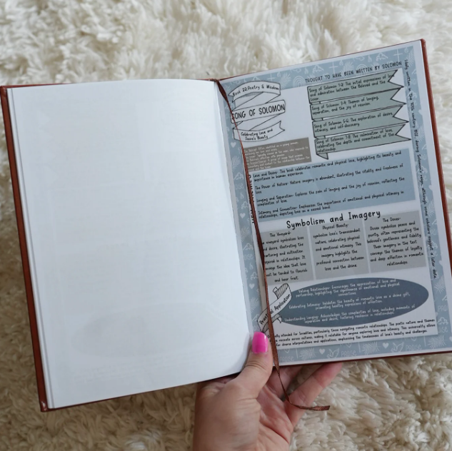A person with pink fingernails holds open a book showing illustrated notes on the Song of Solomon.