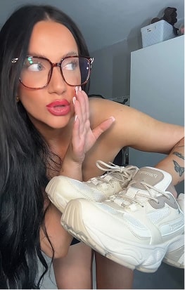 Person with glasses holding a pair of beige sneakers.