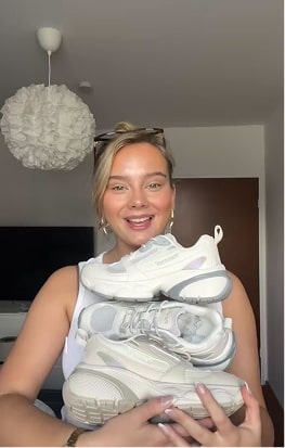 Person holding two pairs of white sneakers indoors.