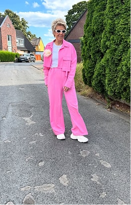 Person in pink outfit and sunglasses standing on a residential street.