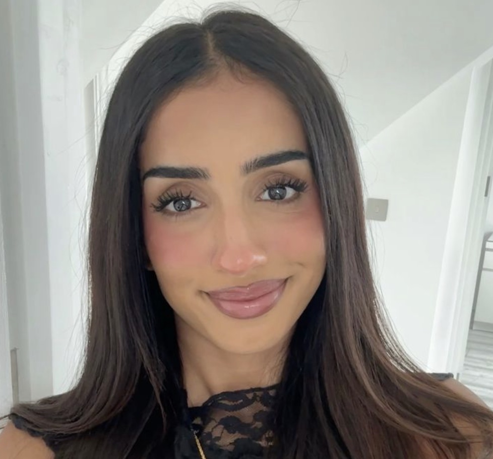 A person with long dark hair smiling indoors.