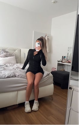 Person sitting on a bed taking a mirror selfie in a bedroom.