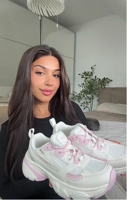 Person holding white and pink sneakers in a bedroom.