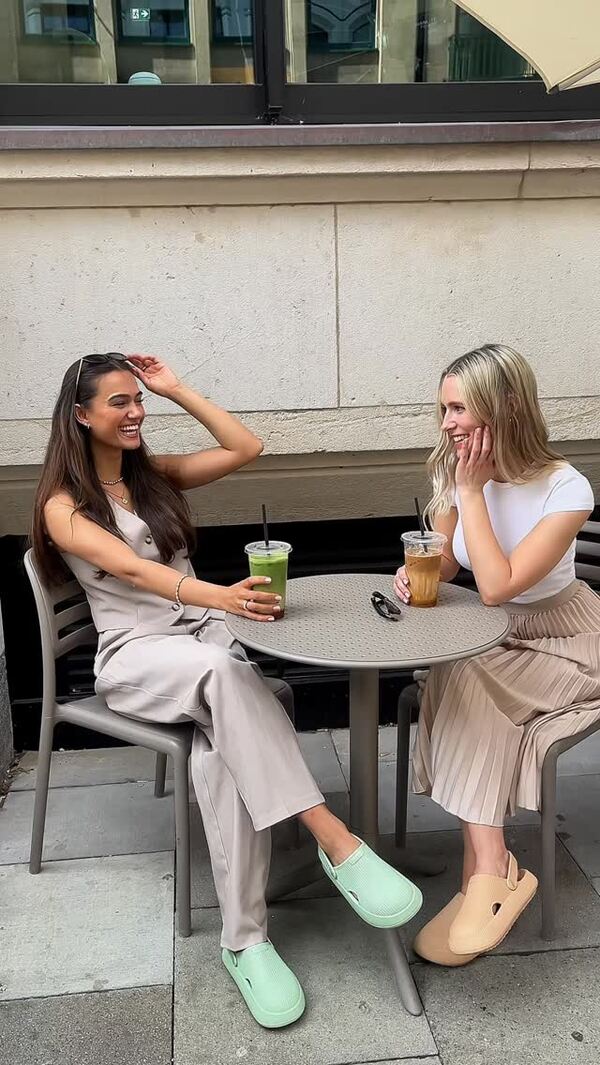 Two women sitting at an outdoor table with drinks, smiling and chatting.
