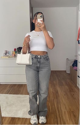 Person taking a mirror selfie in casual outfit with white top and jeans.