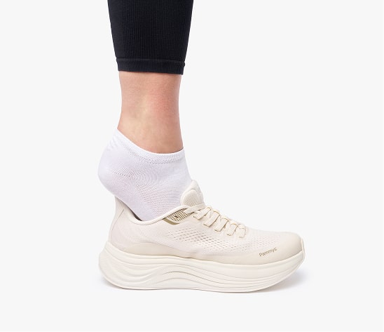Person wearing white socks and beige sneakers on a white background.