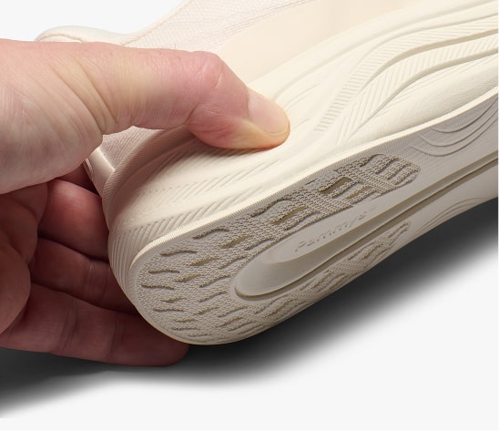Hand holding a white sneaker, focusing on the textured sole.