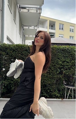 Person in a black dress holding white sneakers, standing outdoors.