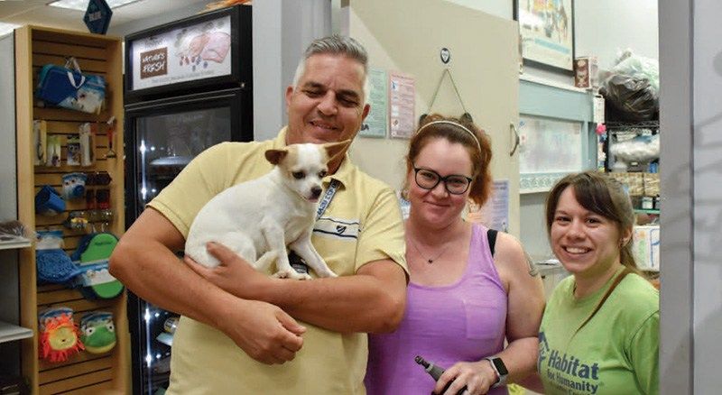 A man holds a small white and tan dog while standing with two smiling women in a store.