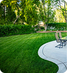 A backyard with a green lawn, patio, and chairs.