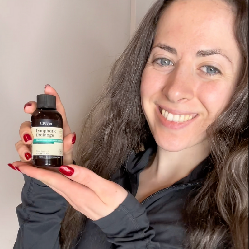 Person holding a bottle labeled 'Lymphatic Drainage' and smiling.