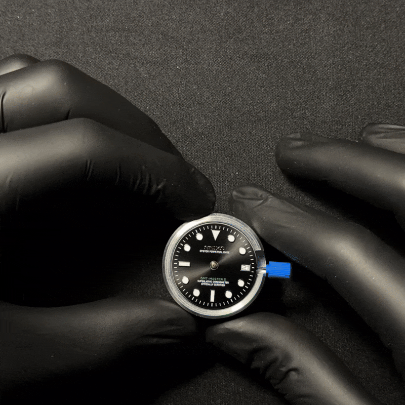 Gloved hands holding a watch face with a black dial.