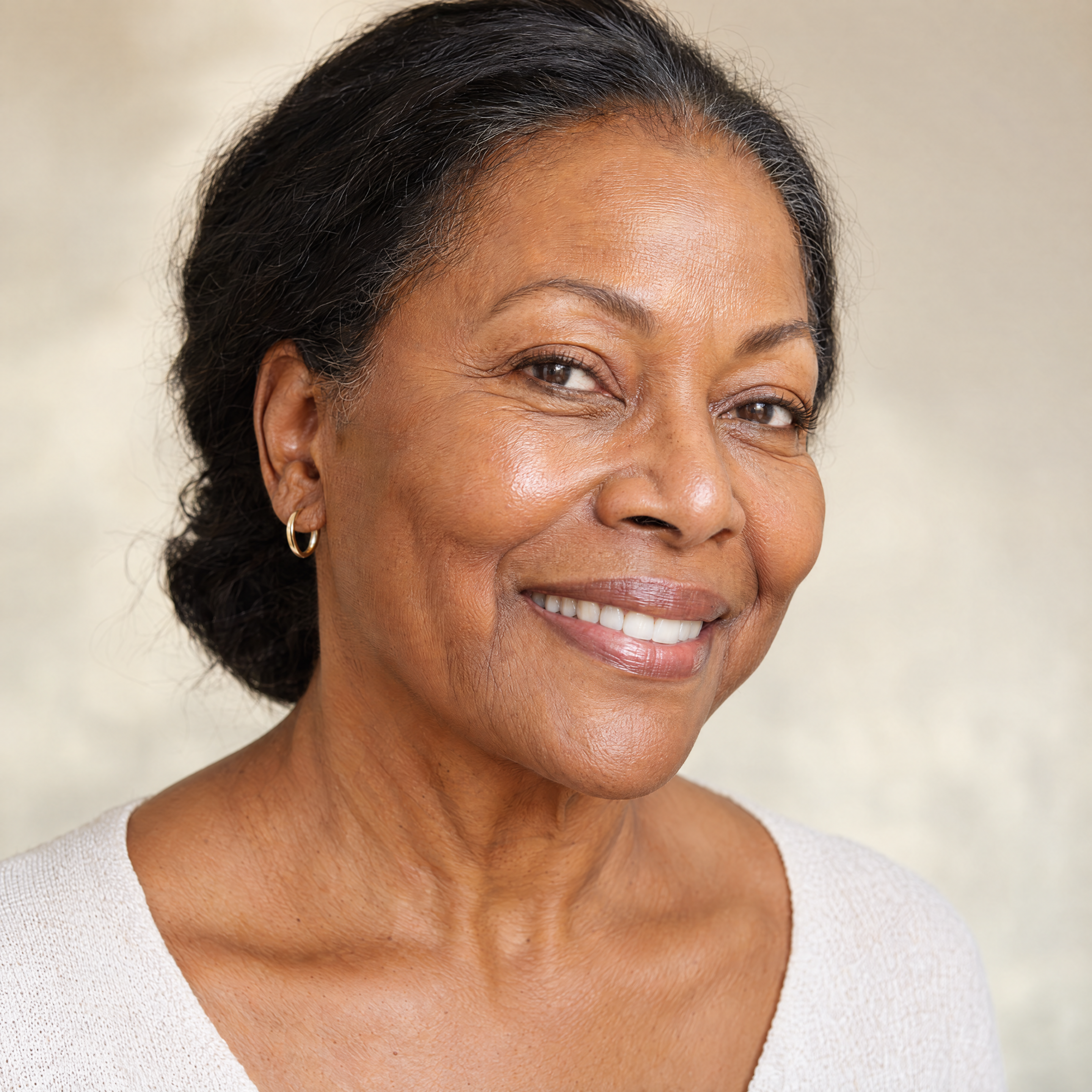 A close-up portrait of a smiling older Black woman with dark hair pulled back against a neutral background.