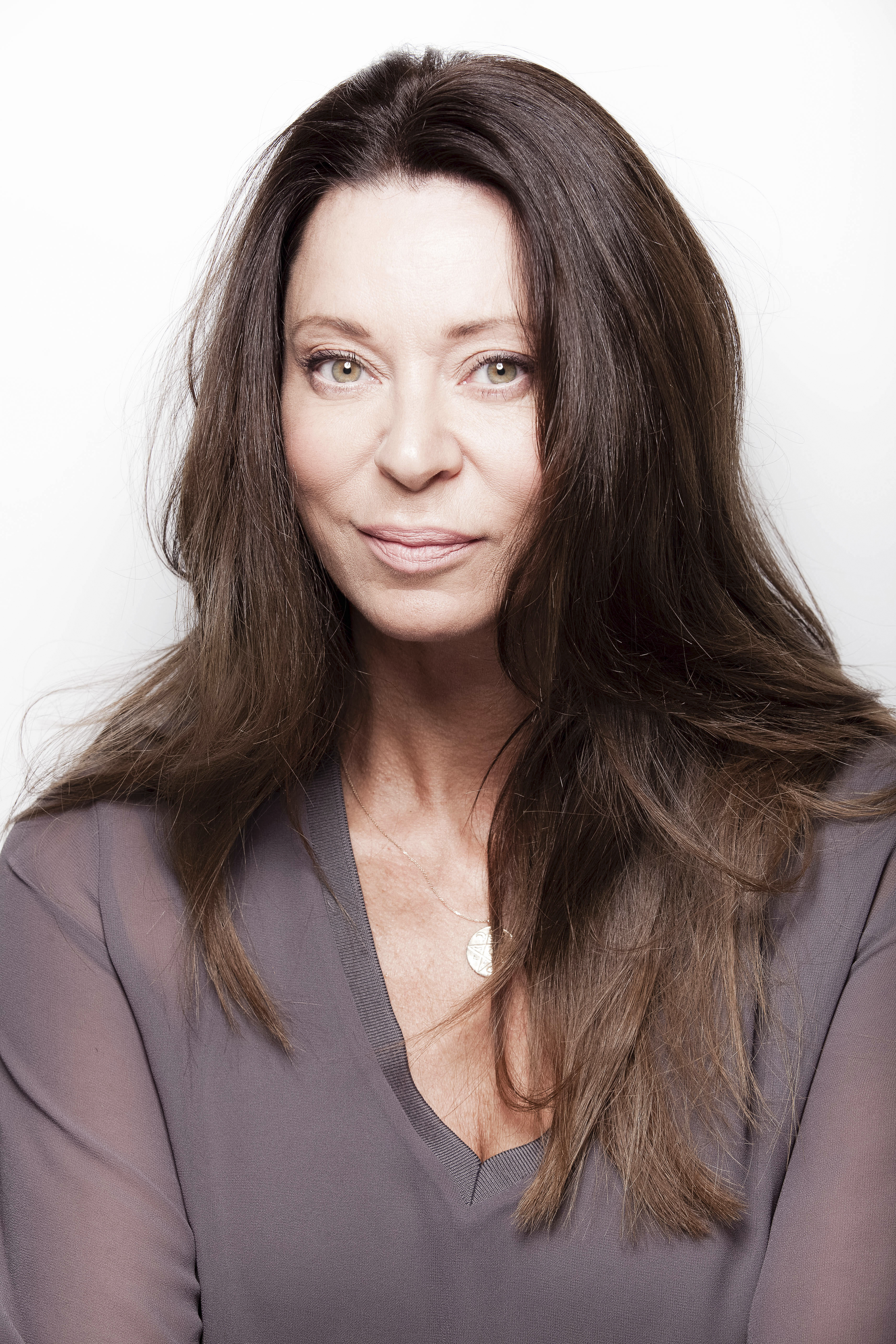A woman with long brown hair wearing a gray top, looking directly at the camera.