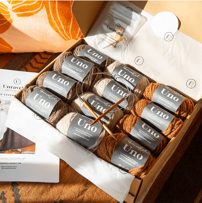 Box of yarn balls with knitting needles and packaging.