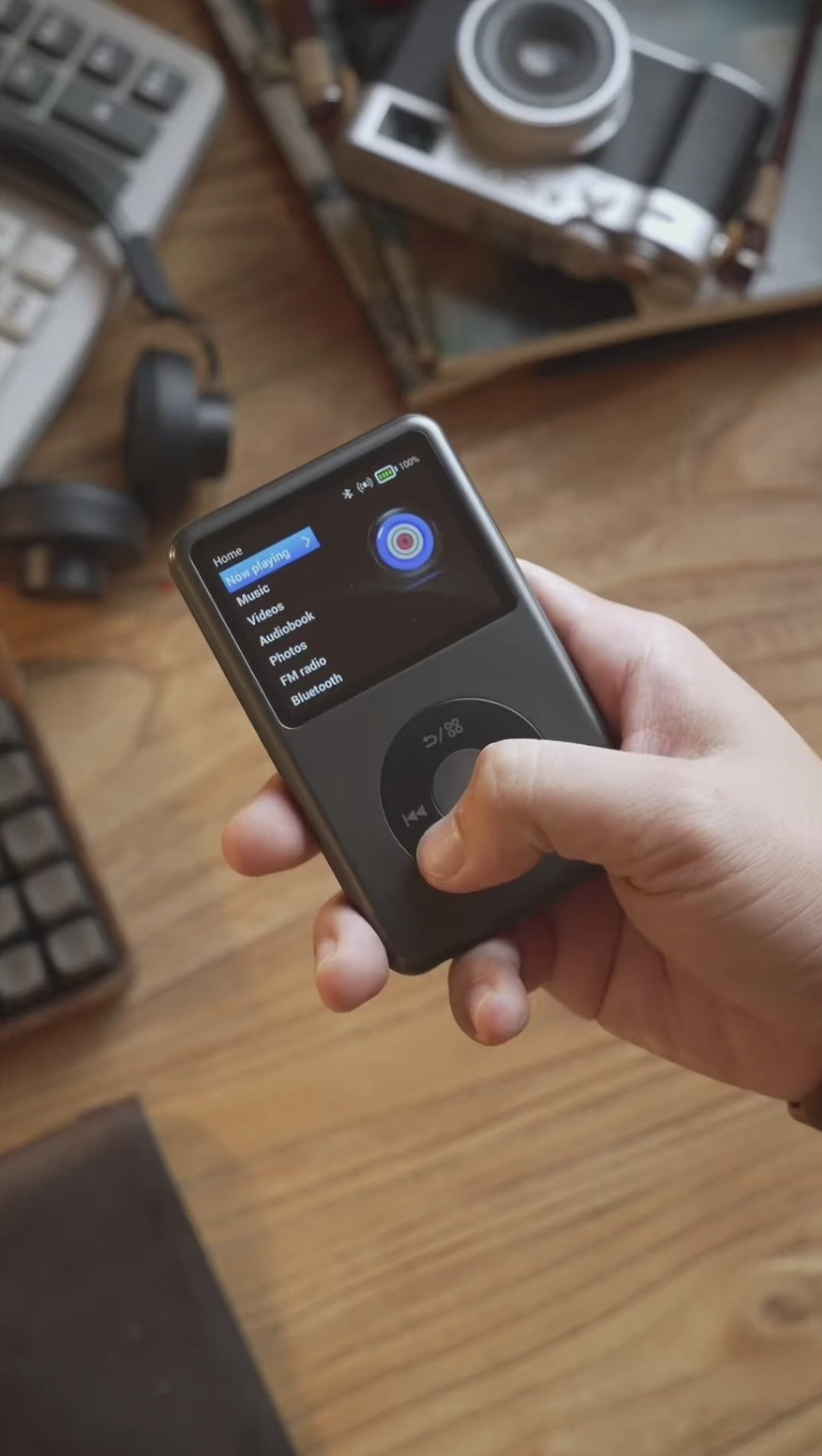 A person's hand holding a gray MP3 player, using the controls to navigate the menu on screen.