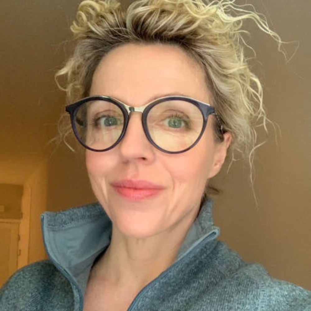 Person with glasses and curly hair smiling indoors.