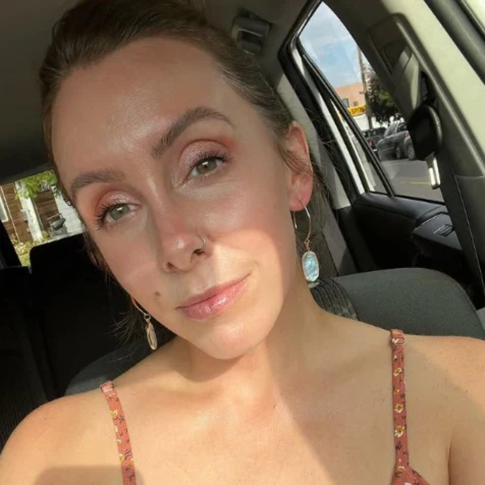 Person sitting in a car, wearing earrings and a floral top.