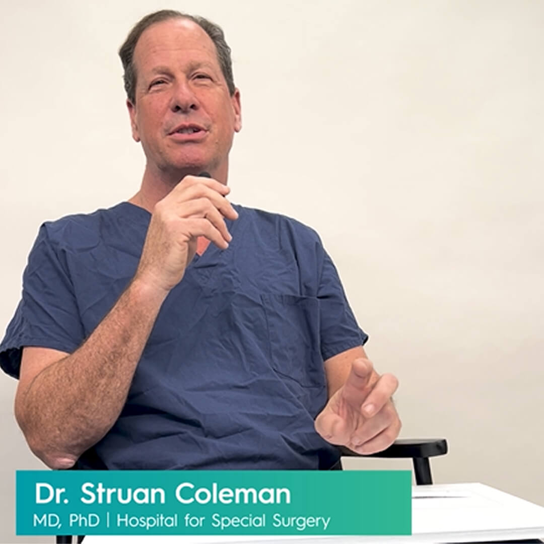 A middle-aged man in blue scrubs, identified as Dr. Struan Coleman, sits and speaks while gesturing.