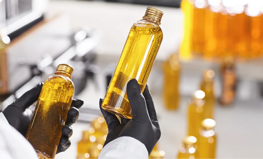 Person wearing gloves holding a bottle of yellow liquid.
