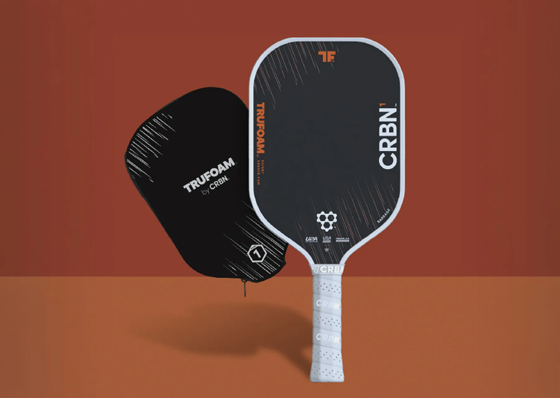 A black CRBN pickleball paddle with a white grip stands next to its black branded protective cover.