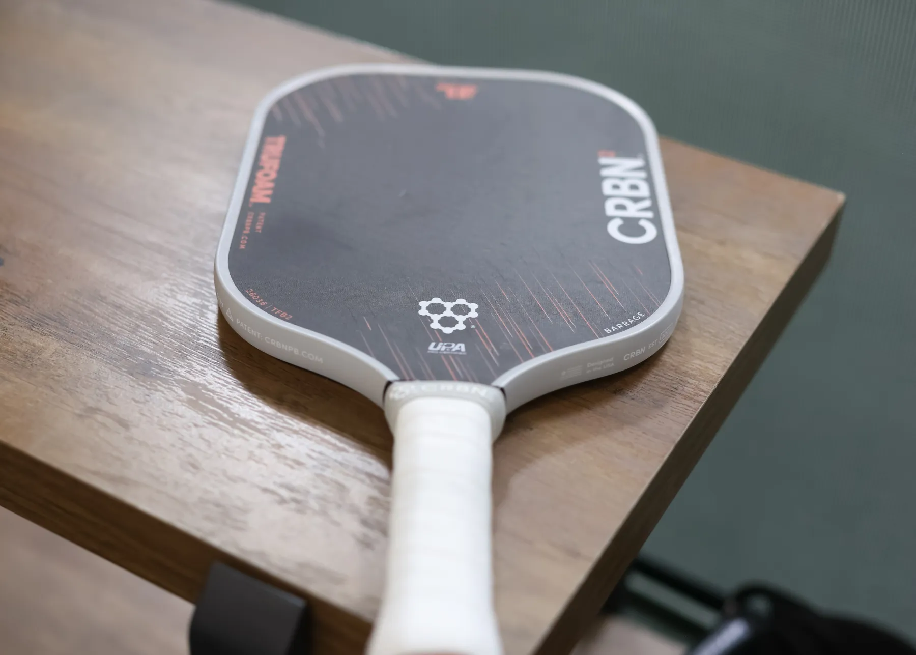 A black and white CRBN pickleball paddle with a white handle resting on a wooden table.