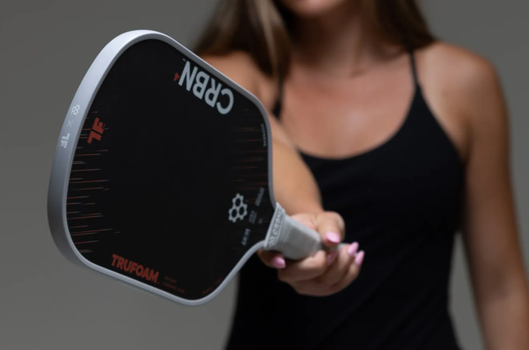 A woman holds a black CRBN pickleball paddle with a white edge guard toward the camera.