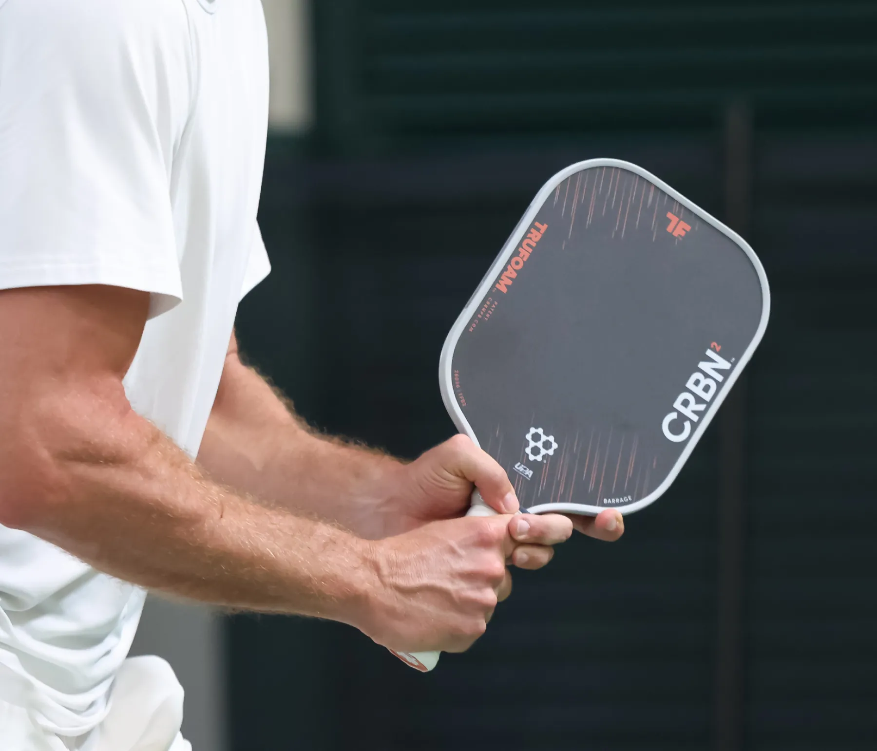 A close-up of a man's hands holding a black CRBN pickleball paddle.