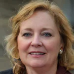 A woman with blonde hair and a warm smile, wearing a dark jacket.