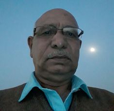 A person wearing glasses and a blue shirt stands outdoors with a moon visible in the background.