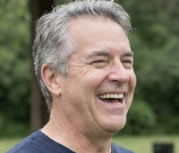 A circular, pixelated photo of a smiling woman with blonde hair in front of a white statue.