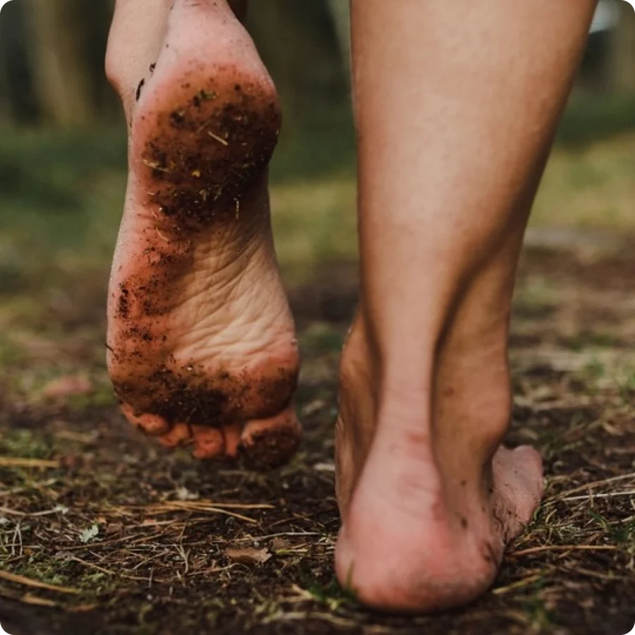 Bare feet walking on a dirt path, one foot lifted showing a dirty sole.