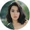 A circular portrait of a young woman with dark, wavy, shoulder-length hair looking at the camera.