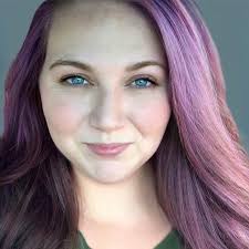 Person with long purple hair and a neutral expression against a plain background.