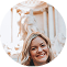 A circular, pixelated photo of a smiling woman with blonde hair in front of a white statue.