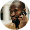 A close-up, circular image of a Black man with a shaved head and beard talking on a smartphone.