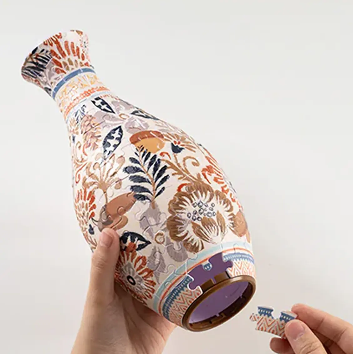 Hands assembling a floral-patterned vase puzzle.