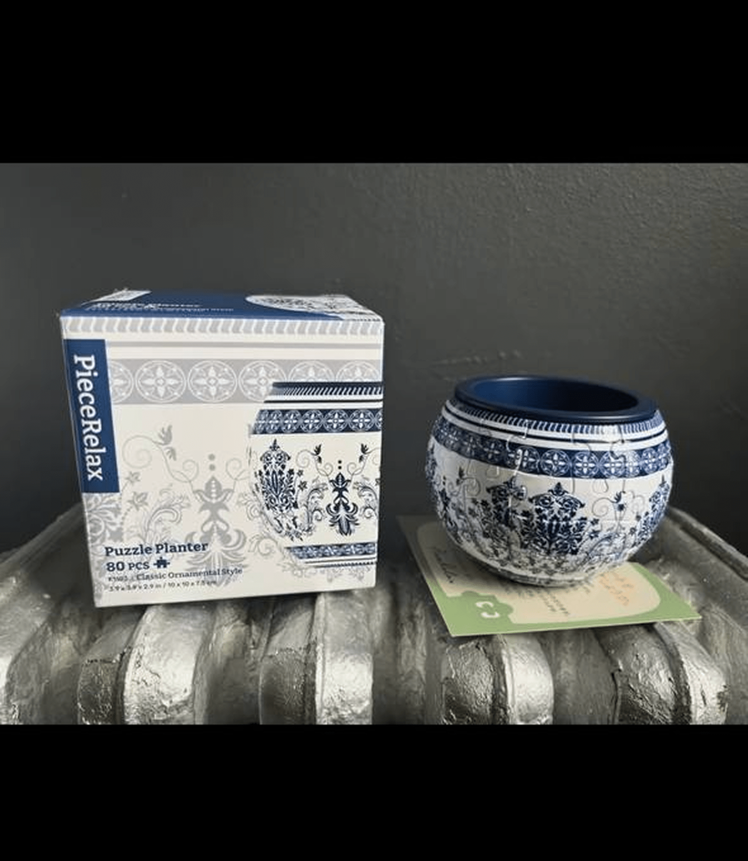 A decorative blue and white puzzle planter with its box on a textured surface.