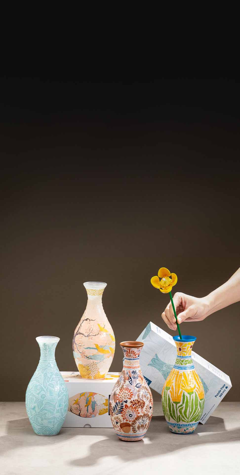 A hand places a yellow flower into one of four colorful, ornate puzzle vases.