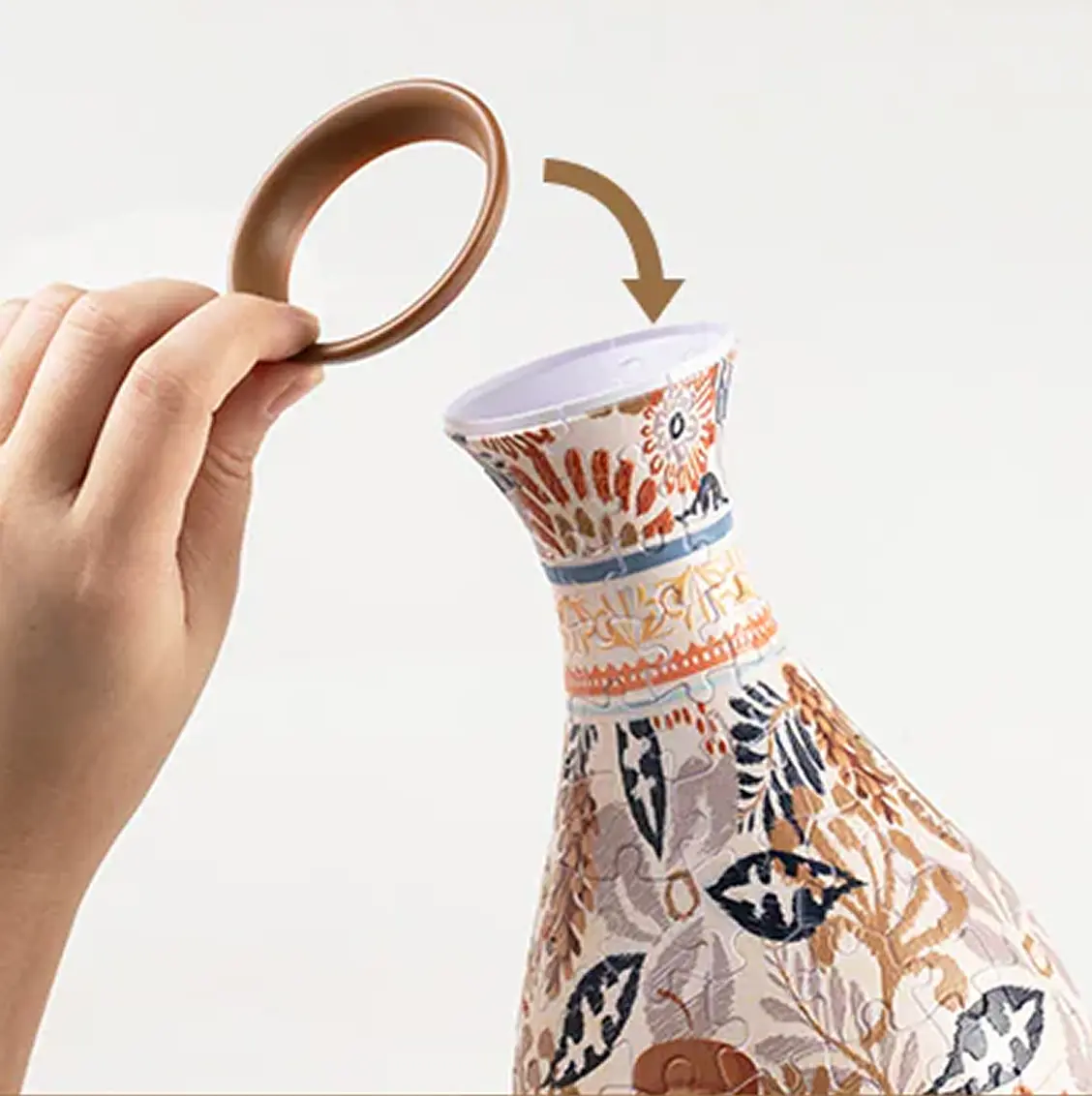 Hand placing a ring on a patterned vase with floral designs.