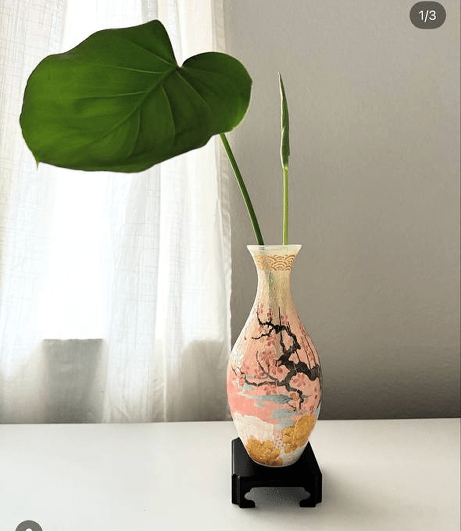 Decorative vase with large green leaf on a white table.