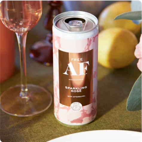 A can of non-alcoholic sparkling rosé on a table with fruits and a glass.