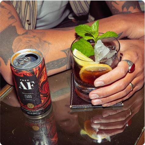 Person holding a garnished cocktail, with a can of Free AF non-alcoholic drink nearby.