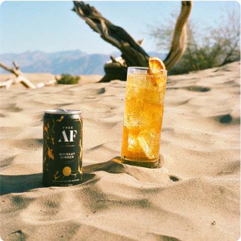 A can of beverage and cocktail on sandy desert terrain.